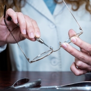 Female optician repairing and fixing eye glasses with screwdriver. Hands holding a mini screwdriver, maintenance and cares service. Frontal view
